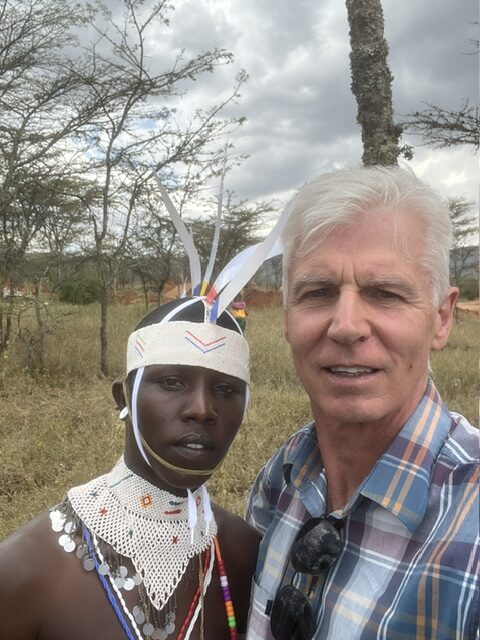 Allan Ward with a young Moran leader in beaded headdress and collar, acacia trees behind them.