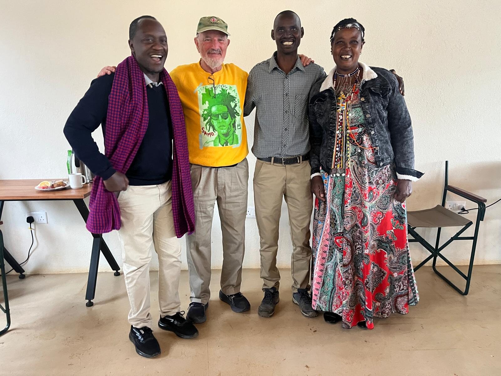Guy Pfeffermann, in a yellow T-shirt and cap, stands arm in arm with trainers Heiz Wadegu, Lavias Lekuuk and Esther Gilisho in a training room.